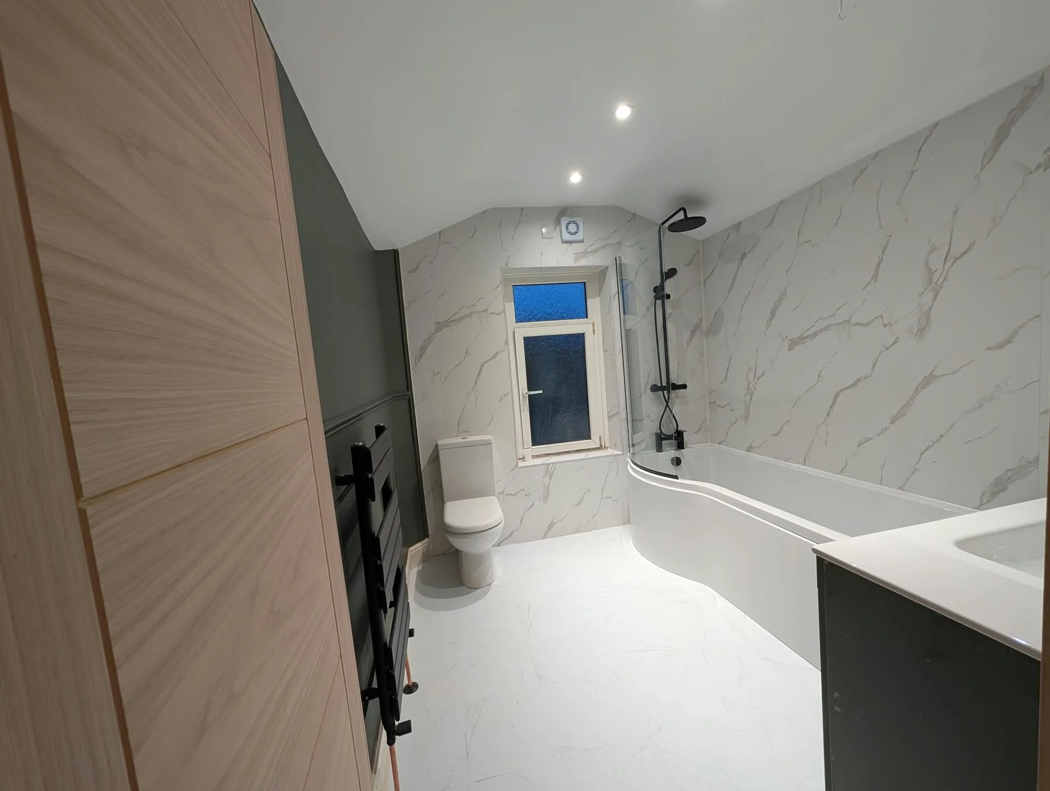 Renovated bathroom with green panelling, black fittings and marble-effect surfaces
