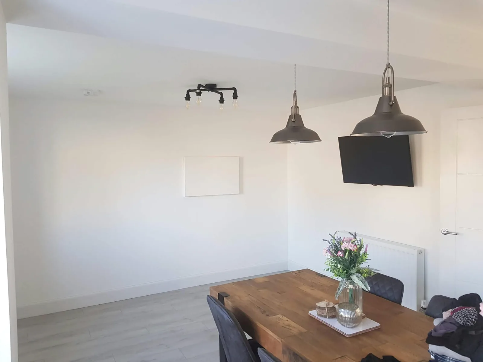 Bright dining room with a timber table, flowers and grey pendant lights.