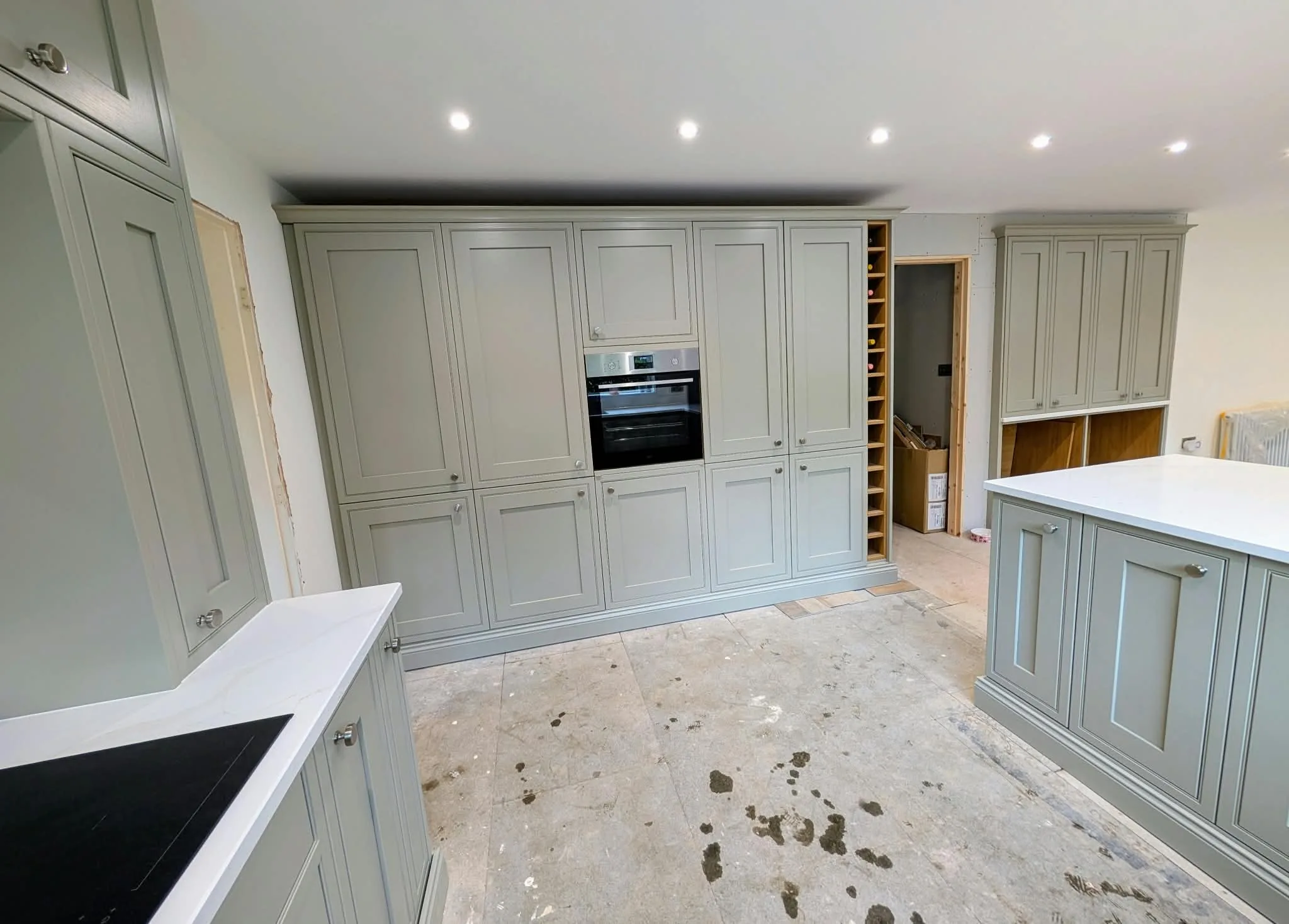 Pale shaker kitchen cabinets and white worktops during installation, before the floor is finished